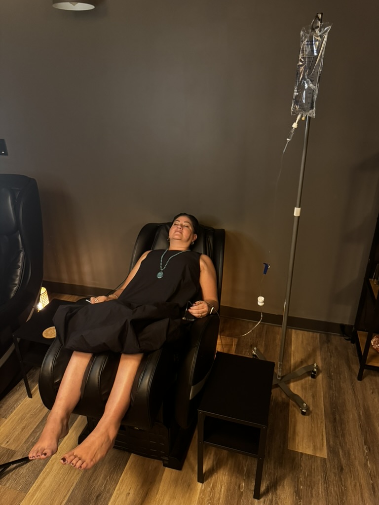 woman in black dress laying in massage chair with eyes closed receiving an IV drip