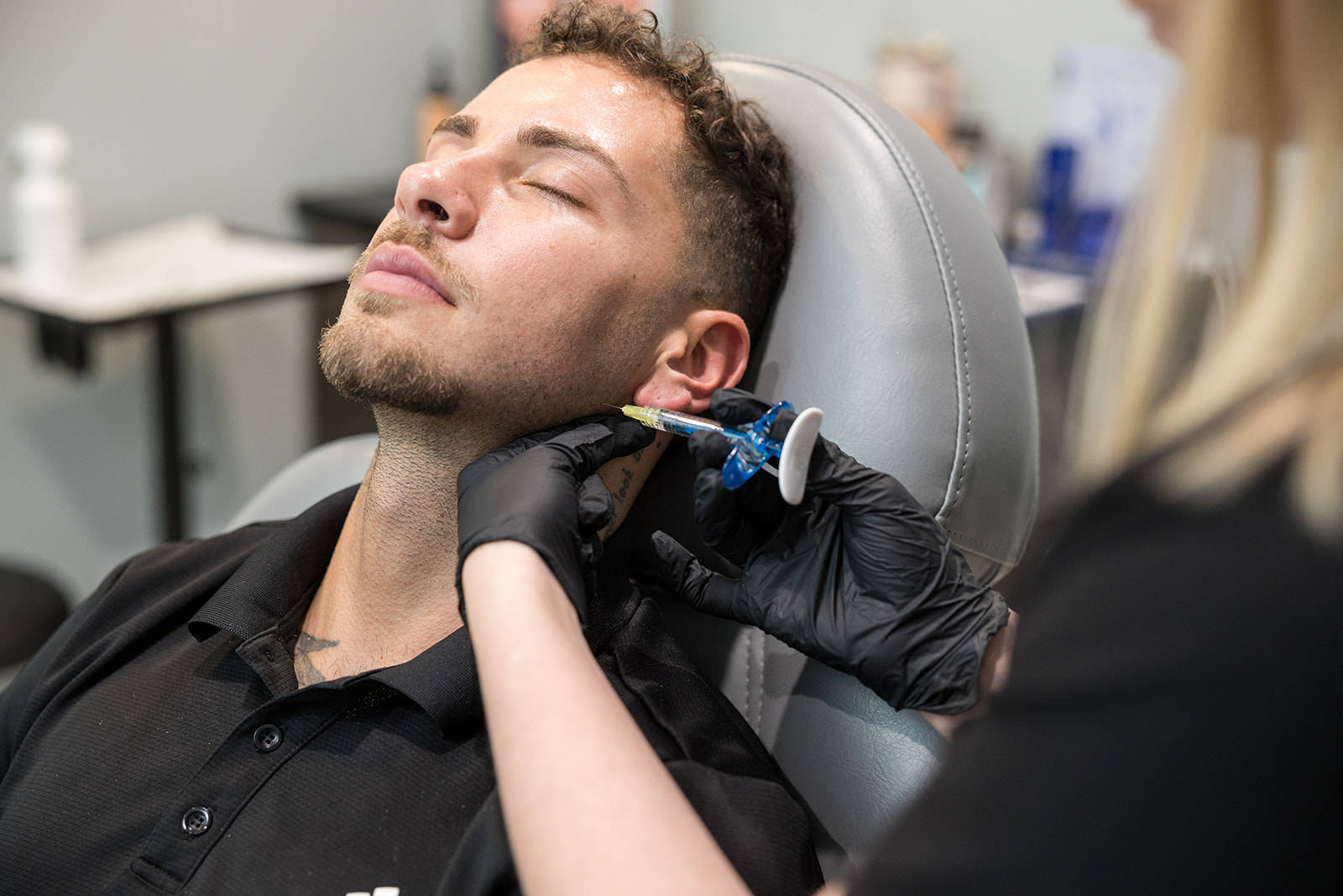 Be Still Wellness man laying on operation table and receiving an injection via needle into his neck from a woman with black rubber gloves